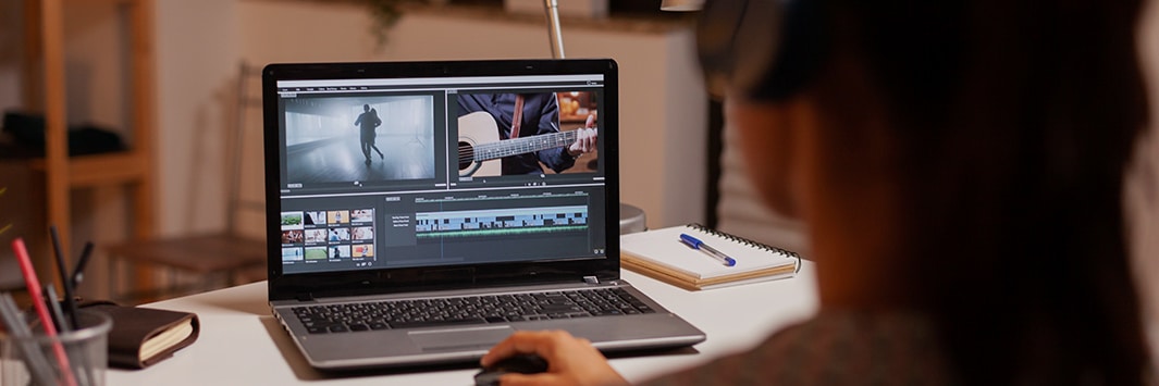 Mano sobre ratón junto a pantalla que muestra una línea de tiempo con pistas de audio y vídeo en un software de edición