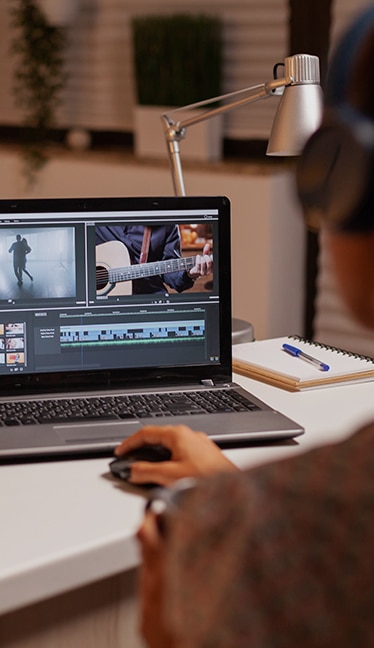 Mano sobre ratón junto a pantalla que muestra una línea de tiempo con pistas de audio y vídeo en un software de edición