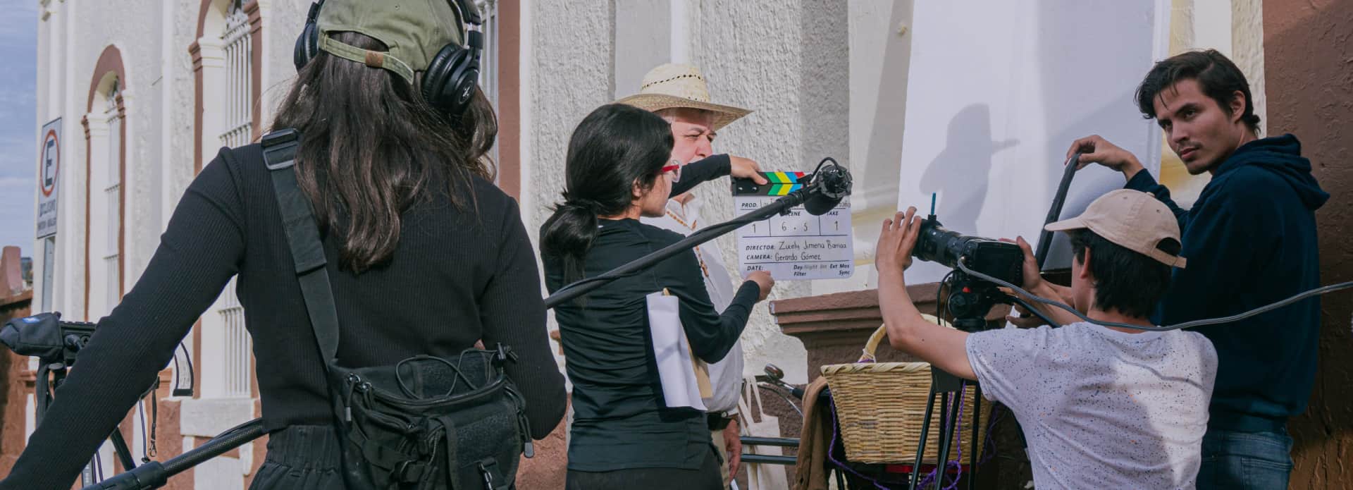 Equipo de rodaje en exterior con cámara, claqueta y micrófono de pértiga durante la grabación de una escena
