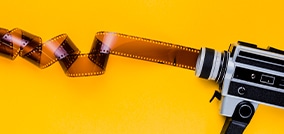 fondo amarillo sobre el que se puede ver una cámara con un carrete de película desenrollado