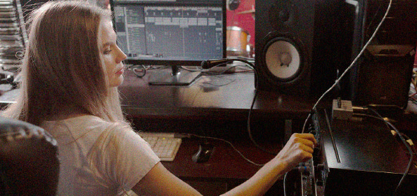 Persona ajusta elementos de un dispositivo de sonido en un estudio de grabación con monitor y altavoces visibles