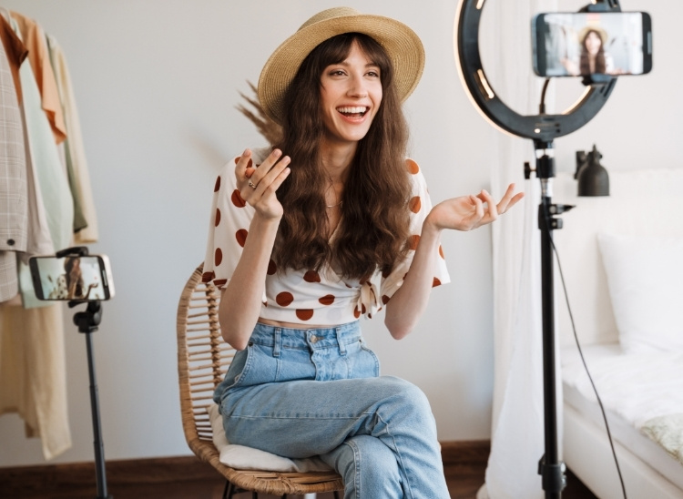 En la imagen, una joven hace reels profesionales como influencer, sentada frente a su smartphone y con un foco de iluminaci&oacute;n